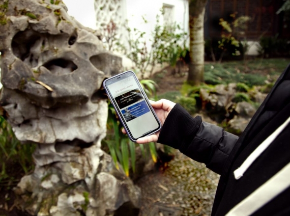 Woman's hand scrolling Discover Lan Su visitor app for audio tour information in front of a free-standing rock. 